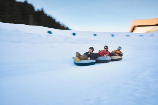group of five people sitting in a row in buoys going down a Tobogganing track