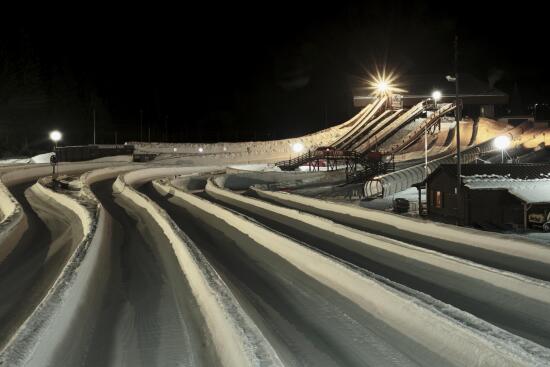 Night view of five Tobogganing tracks with their start in the background and a tunnel track lit from inside.