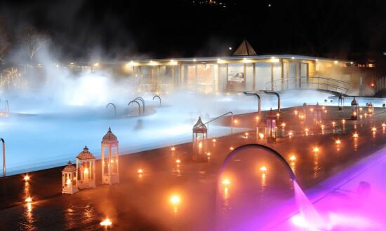 Sur le fond le bleu ciel du bassin, avec la vapeur qui forme une brume. Au premier plan, le bord du bassin agrémenté d'une multitude de lanternes et de bougies allumées