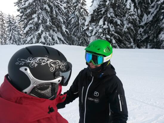 Two skiers chat on a ski run surrounded by trees